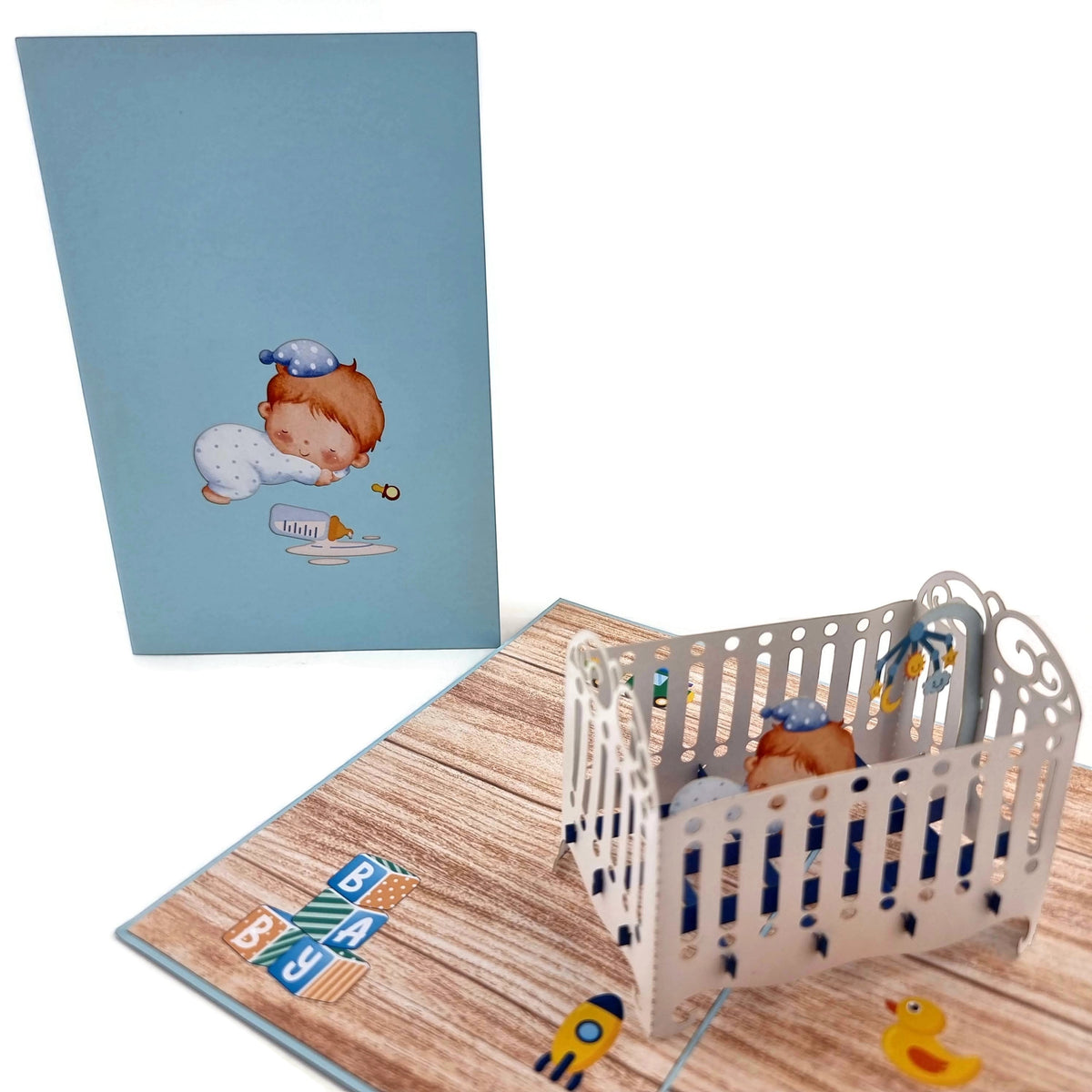 Color Pop Cards blue baby boy crib pop-up greeting card with sleeping baby illustration and 3D cot.
