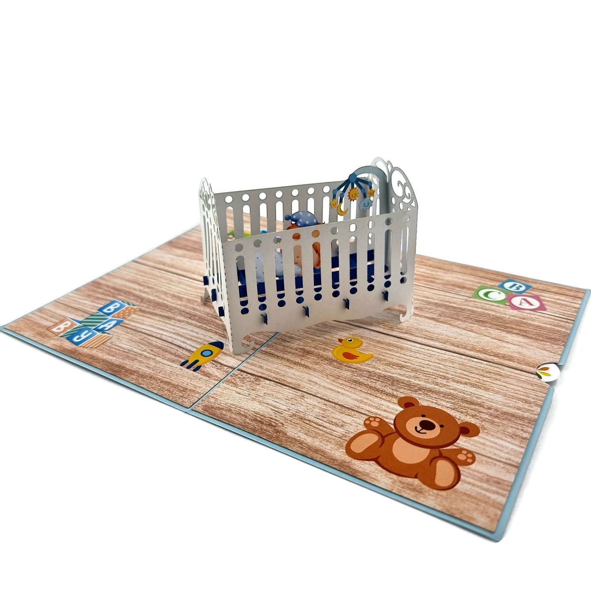 Color Pop Cards blue baby cot pop-up card with 3D crib, sleeping baby, teddy bear, rubber duck, and ABC blocks.