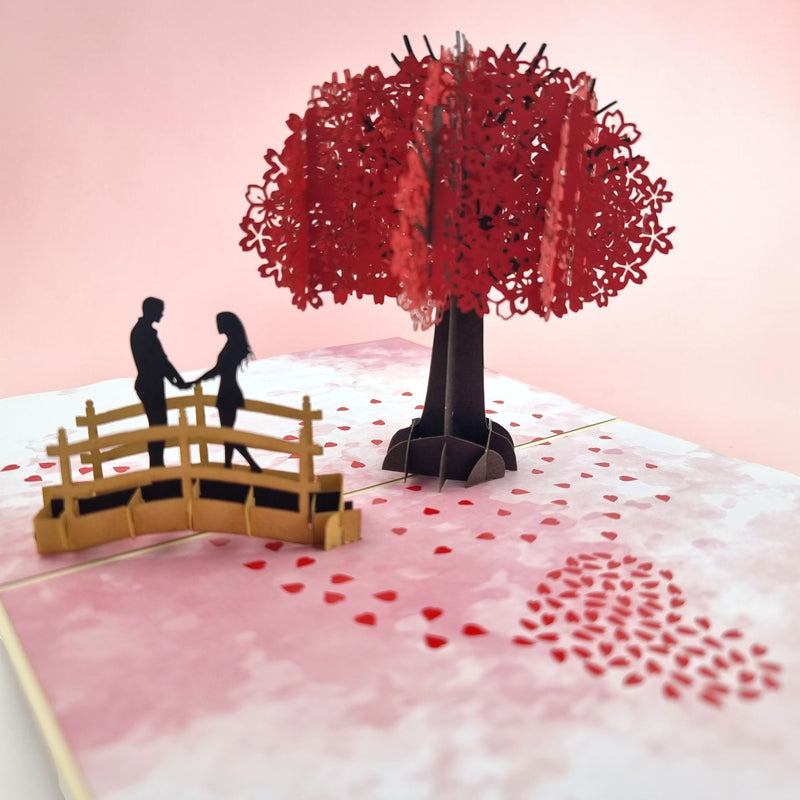 Color Pop Cards Cherry Blossom Love Pop-Up Card with couple on bridge under red tree, red petals form heart.