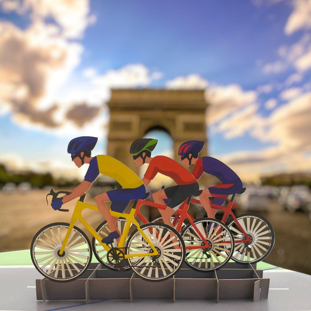 Color Pop Cards cycling race pop-up card featuring three cyclists in yellow, red, and blue racing with the Arc de Triomphe in the background.