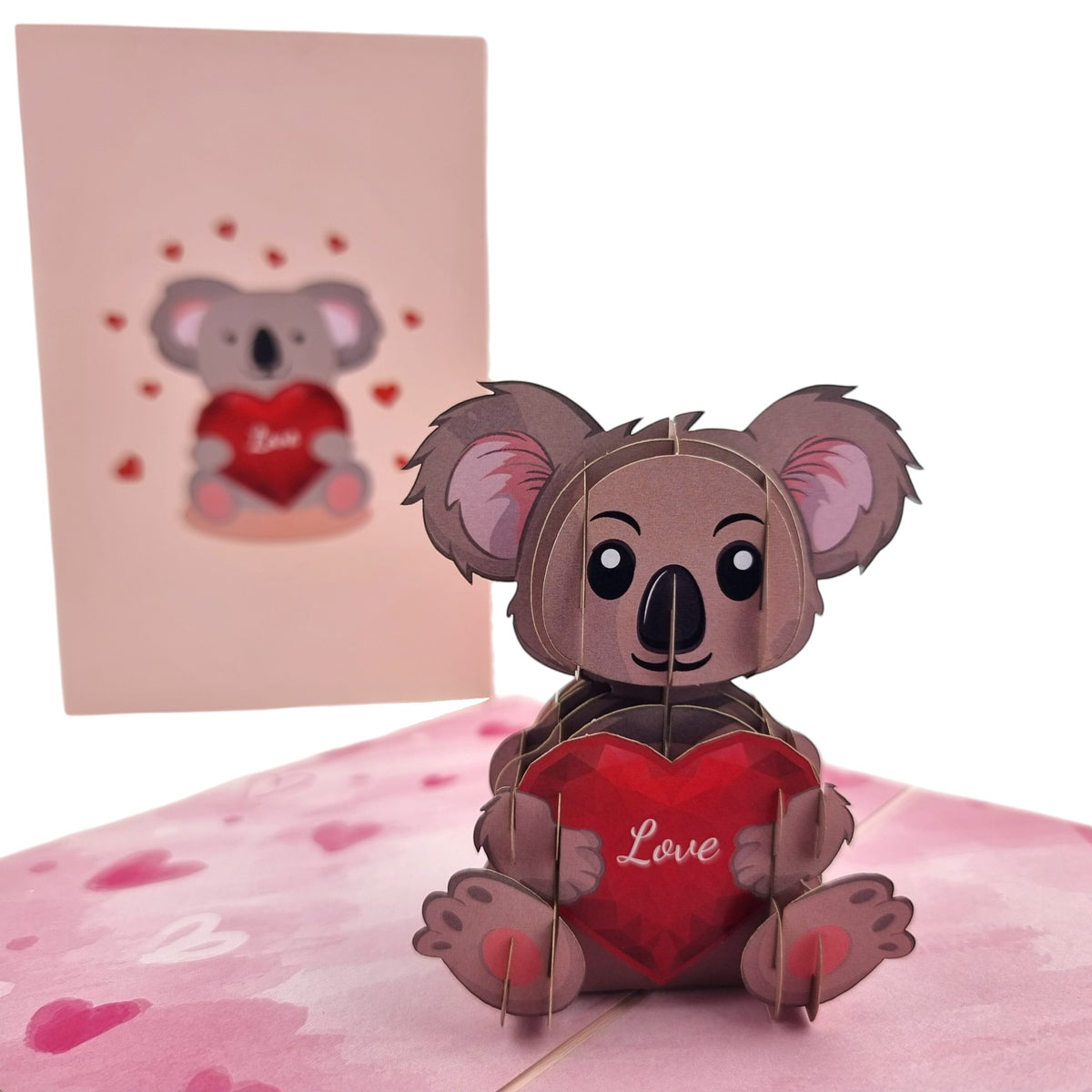 Color Pop Cards pop-up card featuring a brown koala holding a red heart with the word Love. Pink hearts surround the card.