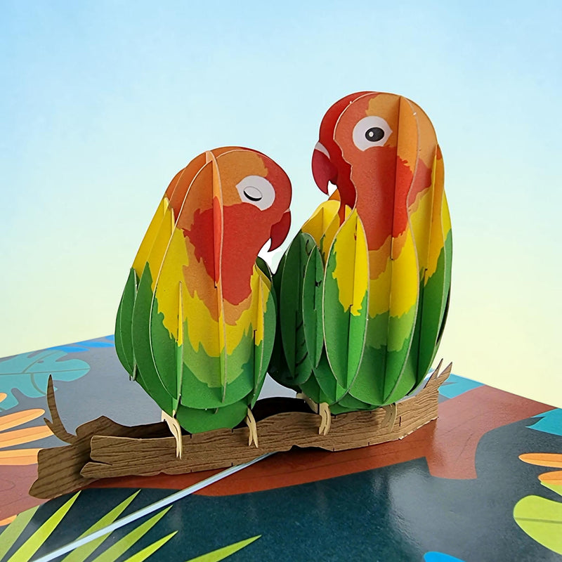 Color Pop Cards Love Birds pop-up card featuring two colorful parrots perched on a branch with flowers. Includes envelope.